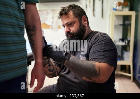 Bearded male artist tattooing on man's hand in studio Stock Photo