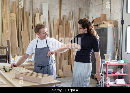 Smiling man and woman giving elbow bump while standing at workshop Stock Photo