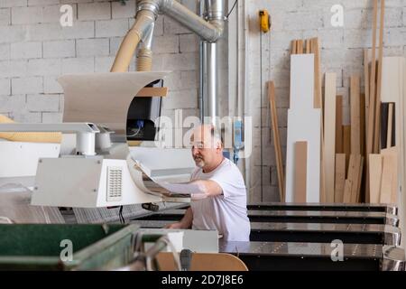 Senior man operating wood cutting machine while sitting at factory Stock Photo
