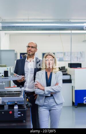Confident mature male and female professionals standing by machinery in factory Stock Photo