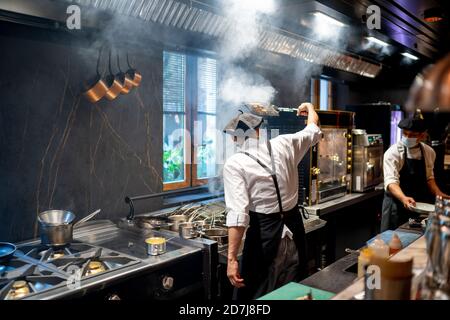 Chefs wearing protective face mask cooking dish in restaurant kitchen Stock Photo