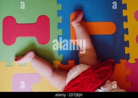 Legs of baby girl lying on colorful puzzle playmat at home Stock Photo