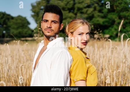 Confident man and woman standing back to back at meadow Stock Photo