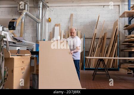 Man operating wood cutting machine while standing at factory Stock Photo