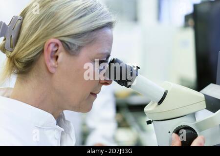 Blond female scientist looking through microscope at illuminated laboratory Stock Photo