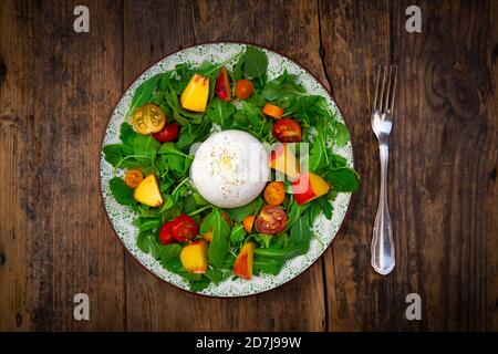 Plate of fresh vegetarian salad with tomatoes, basil, arugula, nectarines, lemon balm and burrata cheese Stock Photo
