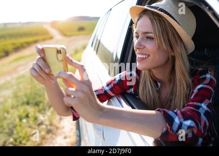 Smiling young woman taking photo through mobile phone while sitting in car Stock Photo