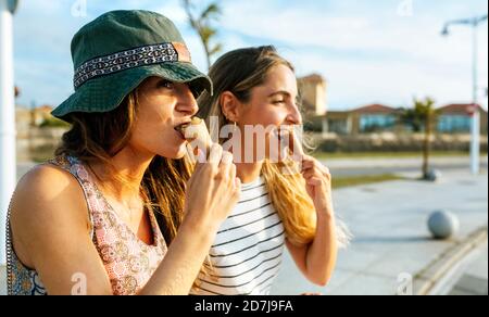 Young women looking away while eating ice cream in city during weekend Stock Photo