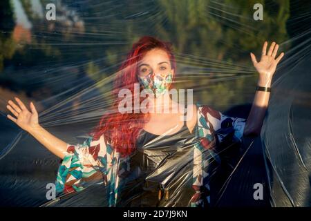 Young woman with protective face mask touching plastic while standing outdoors Stock Photo