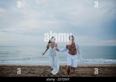 Happy couple holding hands while running on beach Stock Photo
