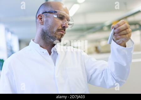 Mature male technician wearing protective eyewear looking at sample in factory Stock Photo