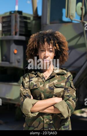 Confident young female army soldier with arms crossed standing against truck at military base Stock Photo