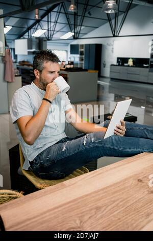 Relaxed businessman looking at digital tablet while drinking coffee in office Stock Photo