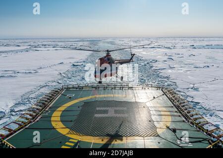 Helicopter landing on helipad of ice-breaker 50 Years of Victory cleaving through ice of Arctic Ocean Stock Photo