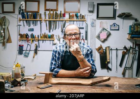 Smiling man with hand on chin standing by workbench at workshop