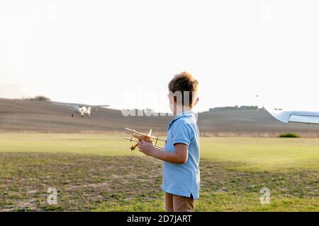 Little boy holding toy airplane while standing at airfield Stock Photo