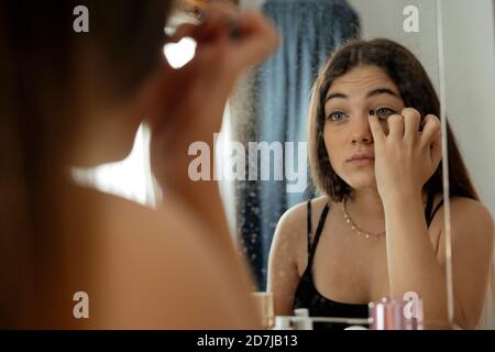Teenage girl applying eyeliner while looking in mirror at home Stock Photo