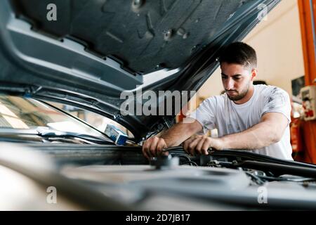 Young man repairing car while standing in auto repair shop Stock Photo