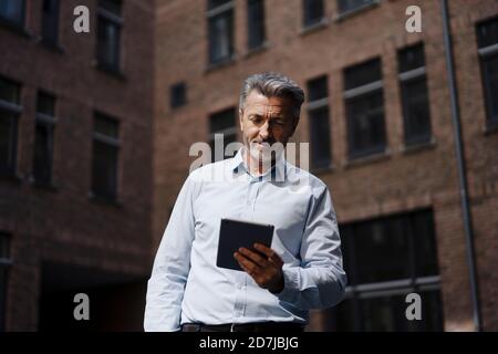 Businessman holding digital tablet while standing against building Stock Photo