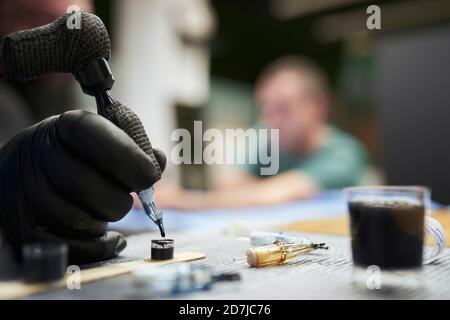 Hand of male artist dipping tattoo machine in ink on table Stock Photo