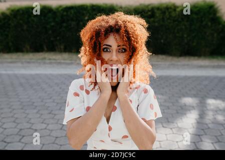 Surprised young woman with mouth open standing on footpath Stock Photo