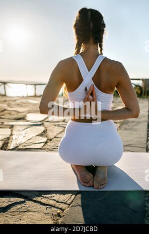 Young woman practicing prayer pose on mat against clear sky at sunset Stock Photo