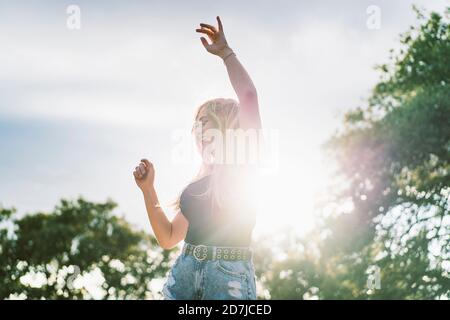 Back lit beautiful young woman dancing against sky Stock Photo