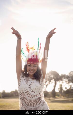 Happy woman wearing Native American Headdress standing with hand raised at park Stock Photo