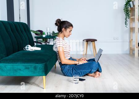 Confident female architect using laptop while sitting cross-legged on floor against sofa at office Stock Photo