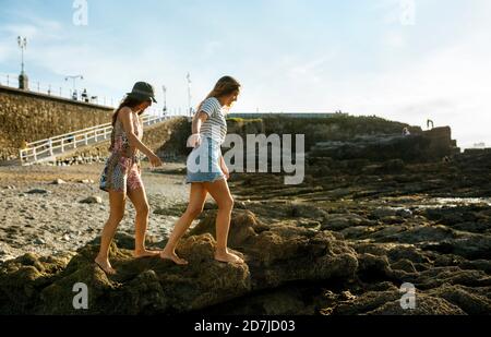 Young women walking on rocks at beach against sky Stock Photo