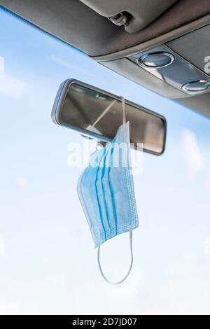 Close-up of face mask hanging on rear-view mirror in car Stock Photo