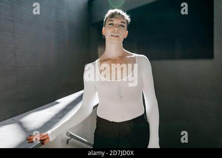 Non-binary young man wearing white leotard standing in basement Stock Photo