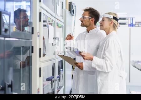 Young male technician analyzing while standing by female colleague at illuminated laboratory Stock Photo