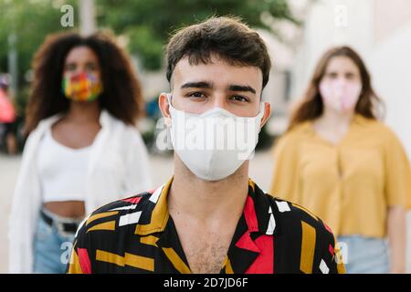 Young man with protective face mask with his friends standing outdoors Stock Photo