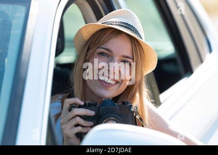 Smiling young woman holding camera while sitting in car Stock Photo
