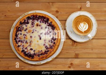 Homemade berry pie with yogurt filling and cup of coffee cappuccino on wooden table. Top view.