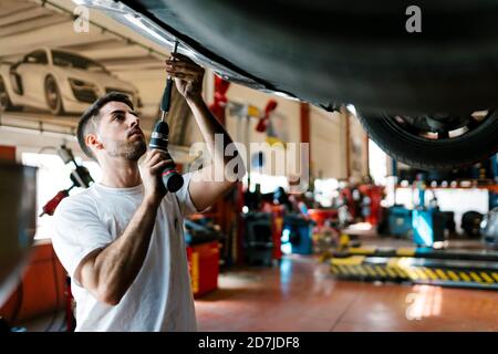 Young mechanic repairing car with work tool in auto repair shop Stock Photo