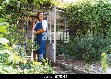 Smiling mature woman holding shovel while standing in back yard Stock Photo