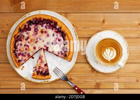 Homemade berry pie with yogurt filling and cup of coffee cappuccino on wooden table. Top view.