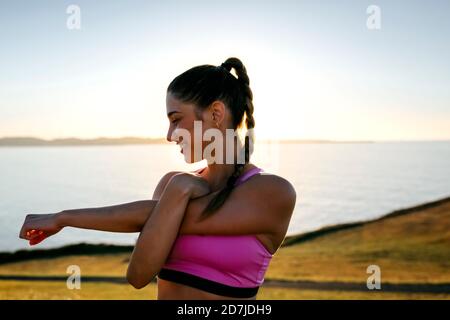 Smiling young woman stretching hands while standing against sea at sunset Stock Photo