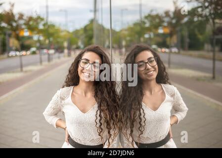 Smiling young woman with long hair standing on sidewalk by modern building in city Stock Photo