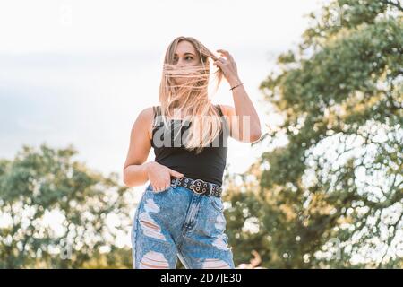 Beautiful young woman with long blond tousled hair standing against sky Stock Photo