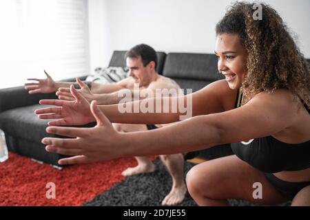 Couple crouching while exercising together at home Stock Photo
