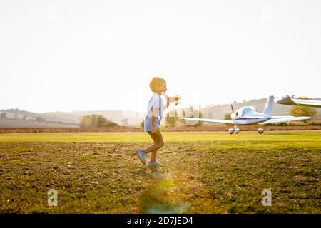 Cute little boy playing with toy plane while standing at airfield on sunny day Stock Photo