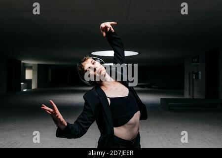 Trans young man listening music over headphones and dancing in illuminated basement Stock Photo