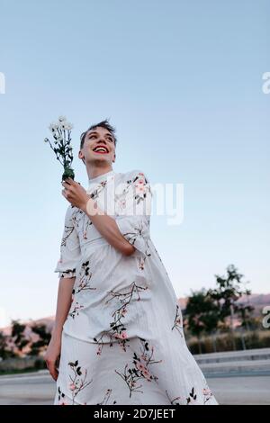 Non-binary male holding bouquet of daisies looking away while standing on street Stock Photo