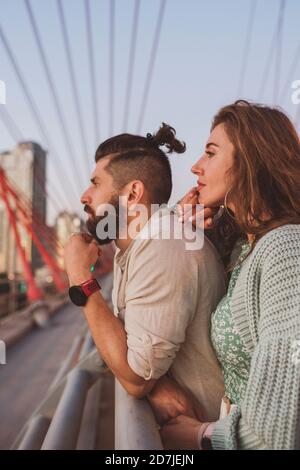 Thoughtful boyfriend and girlfriend looking away while standing on bridge in city Stock Photo