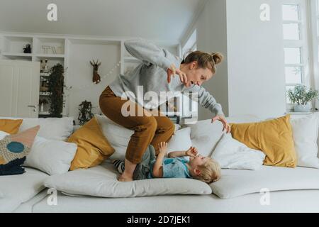 Mother gesturing while standing on sofa by boy at home Stock Photo