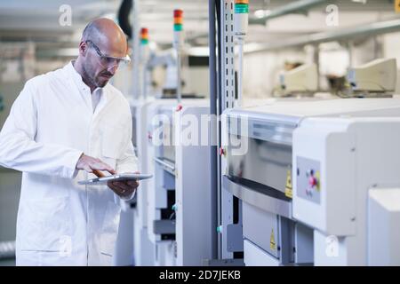 Mature male technician using digital tablet while examining machinery at laboratory Stock Photo