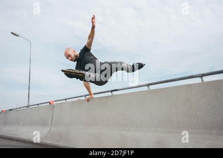 Carefree young man with inline skates jumping over railing on bridge Stock Photo